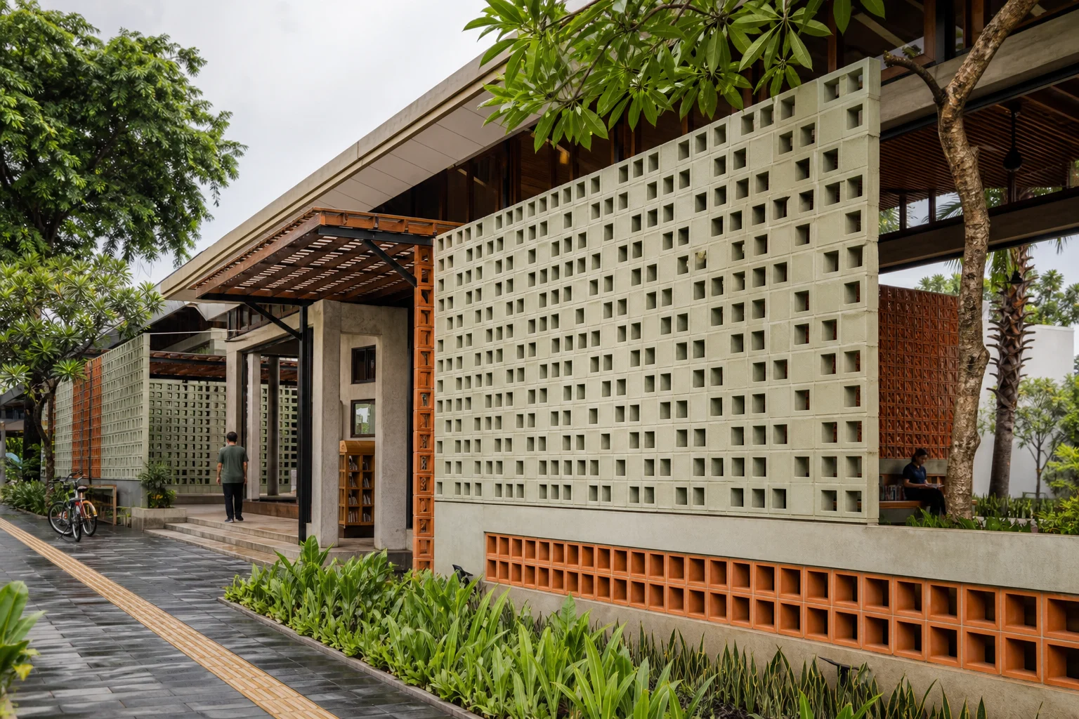 Masonry berlubang warna sage dan terracotta menaungi perpustakaan komunitas tropis kontemporer.